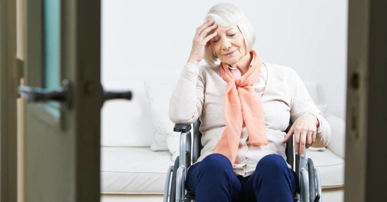 Senior Women in wheelchair at nursing home holding her head