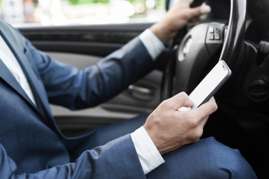 Man in a suit looking down at his phone while driving a car