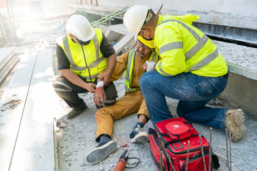 An injured construction worker being helped by two coworkers