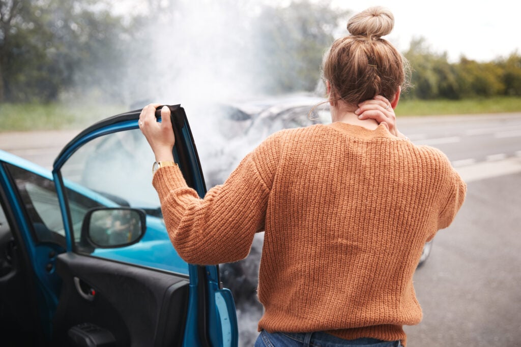 Woman stepping out of a car rubbing her neck in pain after a car accident