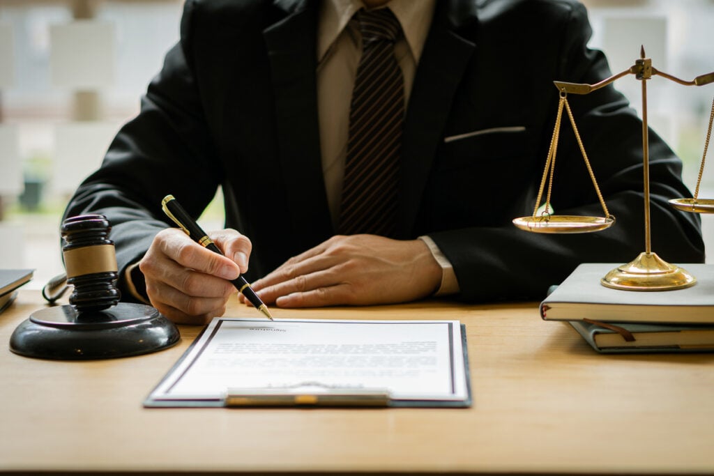 Male lawyer signing paperwork at a desk with with a gavel and scales
