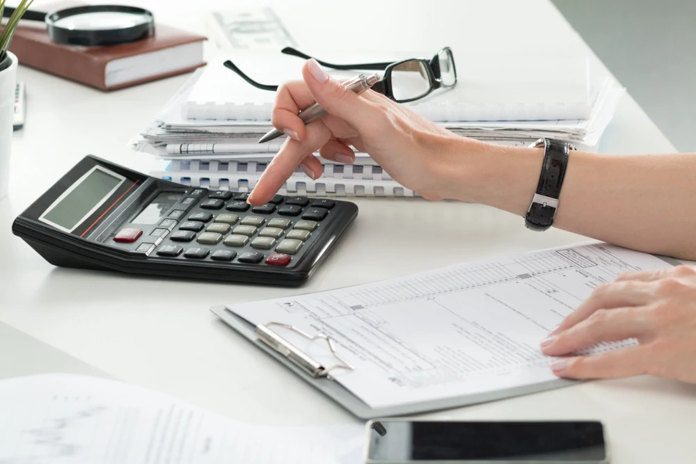 Person with a clipboard and calculator filling out a form