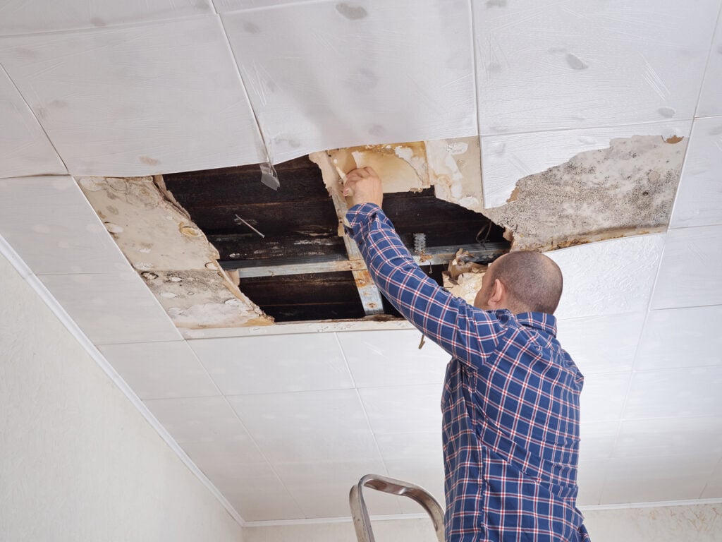 A man in a blue shirt working to repair a collapsed ceiling
