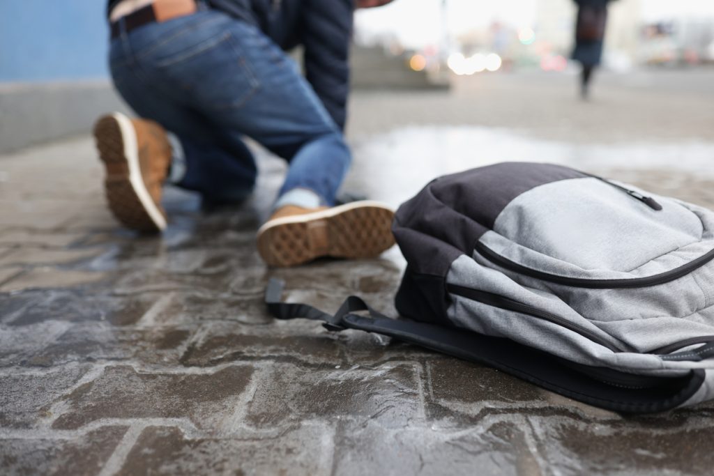 Man with backpack slipping and falling on a wet sidewalk