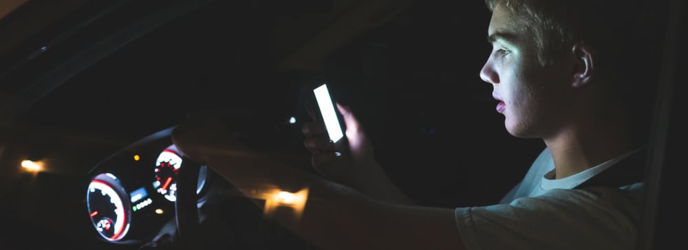 Teenage driver looking at his phone while driving at night