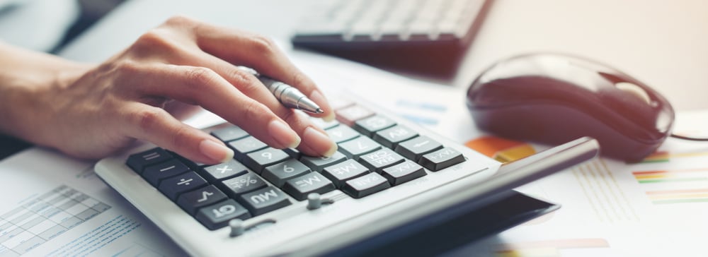 Close up of a person using a calculator on top of documents