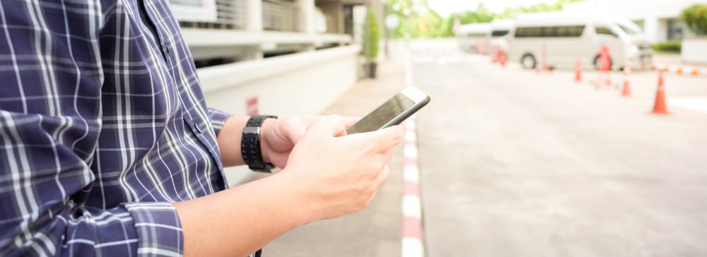 A man standing on the curb using his phone to call a rideshare service