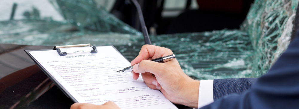 An insurance adjuster with a clipboard examining the scene of a car accident