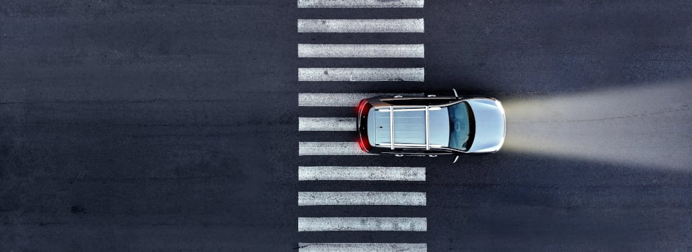 Aerial view of a car with its headlights on driving over a pedestrian crosswalk at night.