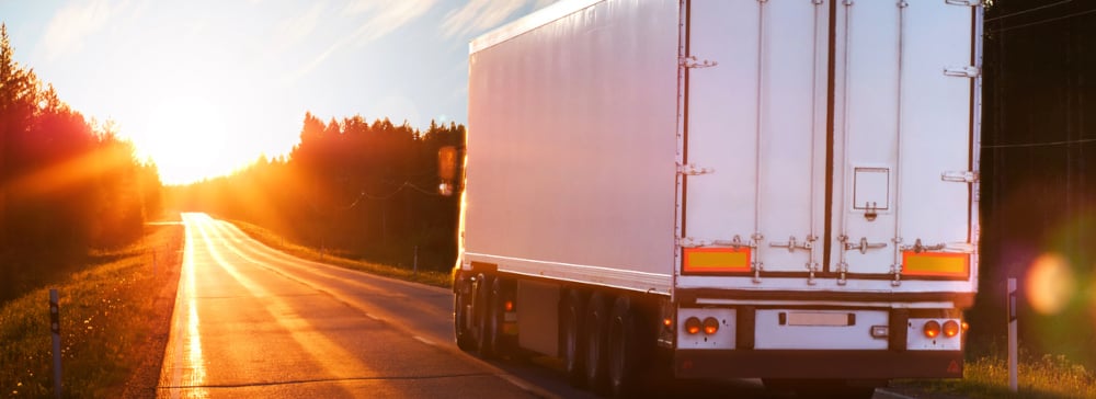 A white semi-truck driving down the road towards the sun