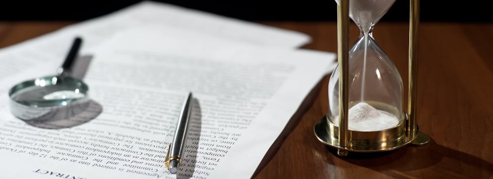 Close-up of an hourglass, pen, and magnifying glass on top of a legal document