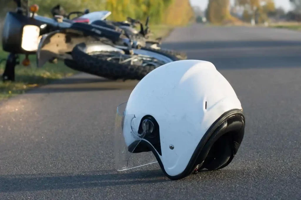 White helmet laying in front of a fallen motorcycle on the side of the road.