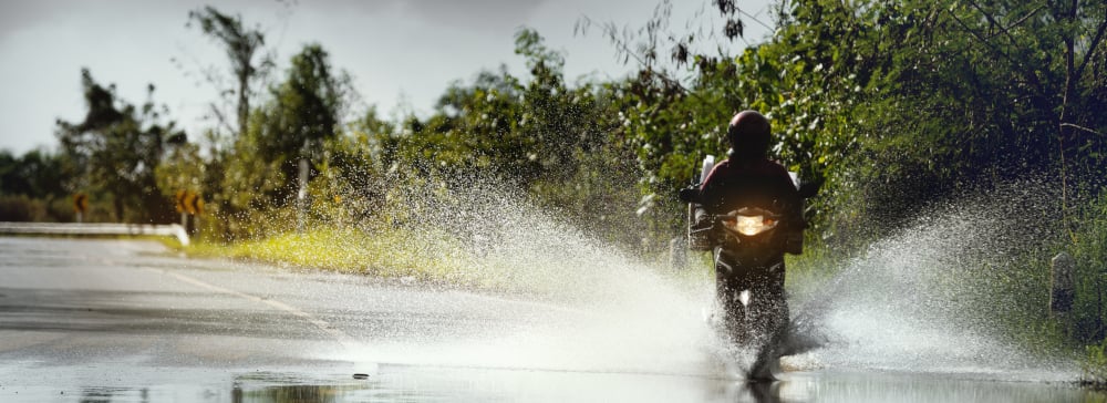 Person driving a motorcycle through floodwaters on the side of the road