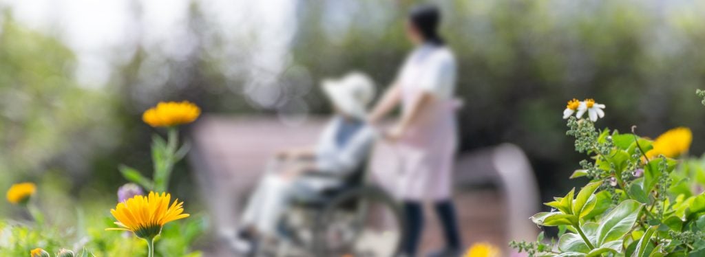 Nursing home nurse pushing a woman in a wheelchair through a garden