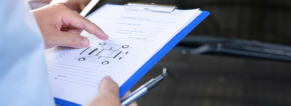 An insurance claims adjuster with a clipboard examining a damaged car