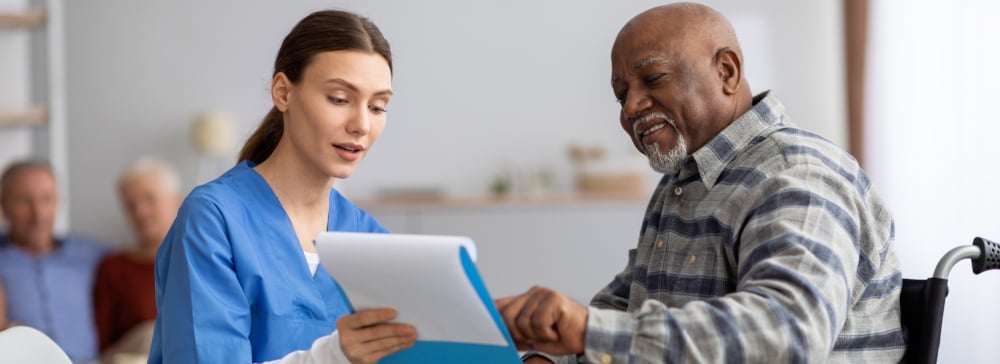 Nursing home attendant speaking with an elderly man in a wheelchair