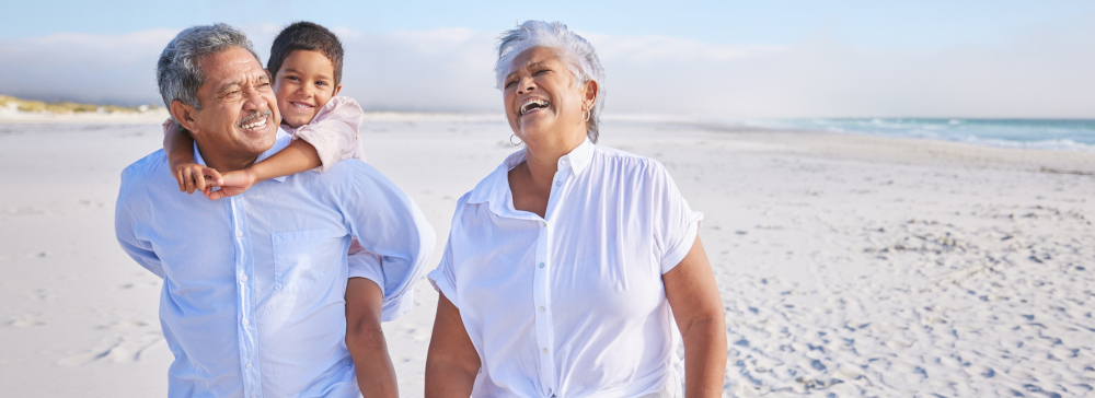 Two grandparents and their grandchild laughing and walking on the beach