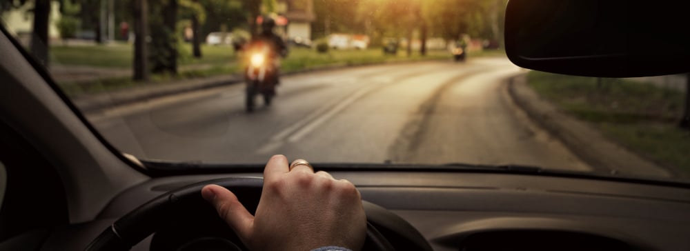 A view from the drivers seat of a motorcycle approaching a car on the street