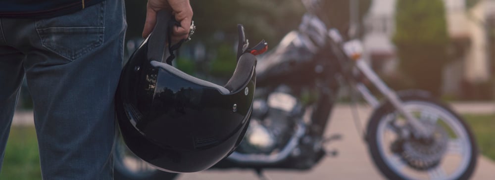 Motorcycle rider holding a helmet facing a black motorcycle