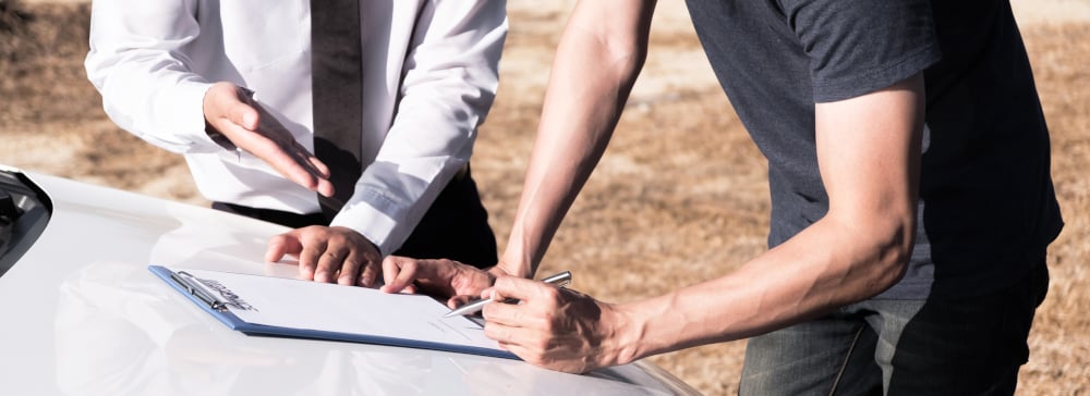 Insurance agent and car owner signing paperwork for an accident claim on the hood of a car