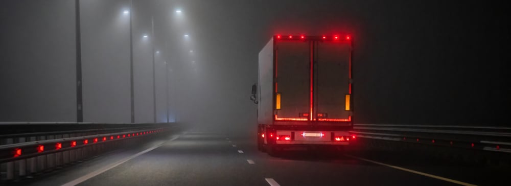 A truck with red running lights driving on a foggy highway at night