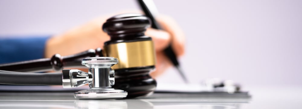 A person signing a piece of paper with a gavel and stethoscope in the foreground