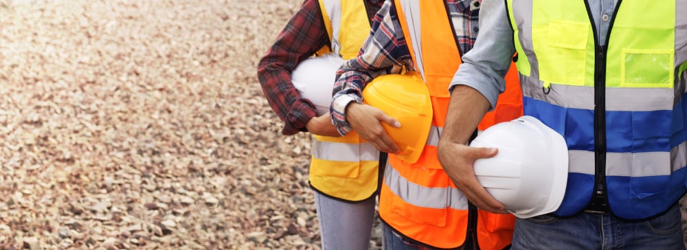 Three construction workers in a line wearing safety vests and holding their hard hats