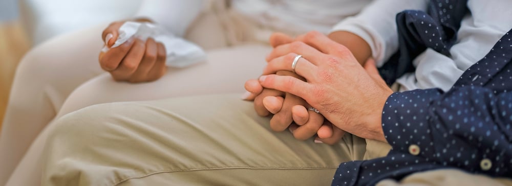 Two people holding hands and grieving on a sofa