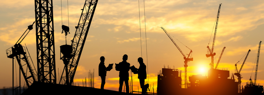 Silhouette of construction workers standing on a construction site with cranes and a sunset in the background
