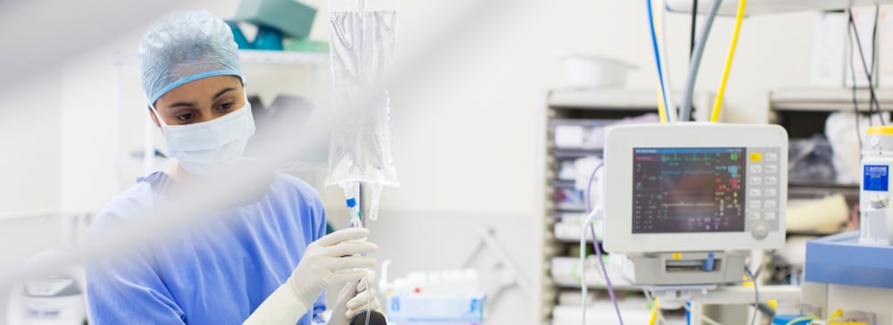 A nurse with an IV bag standing in an operating room with medical equipment