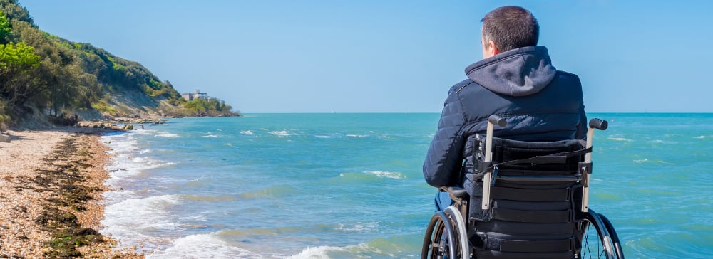 Back of a paralyzed man sitting in a wheelchair looking at the ocean