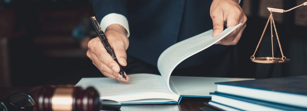 An attorney writing in a notebook next to a gavel and scales representing the law