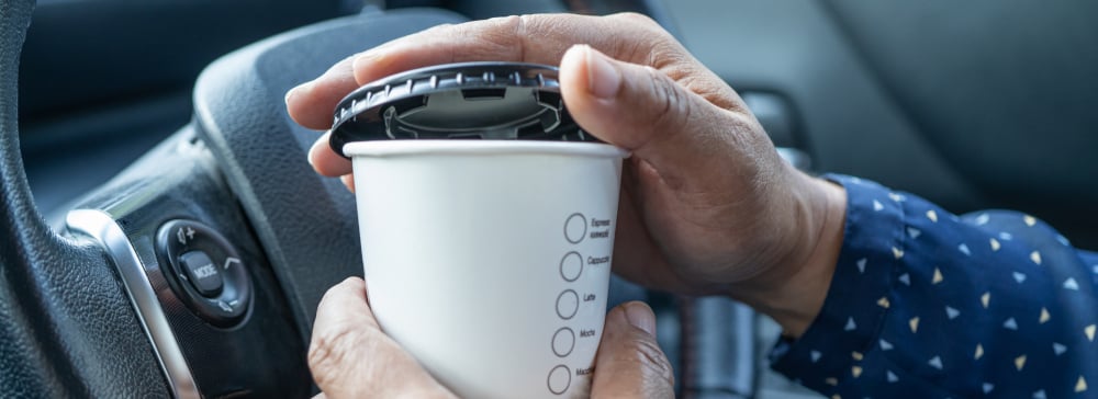 A person opening a coffee cup while driving their car