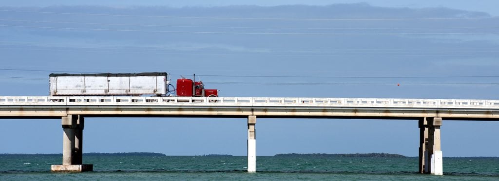 A distant shot of a red semi-truck driving over a bridge over water in Florida