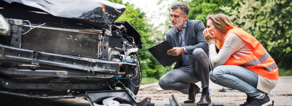 A woman and a truck accident lawyer with a clipboard examine a crashed truck