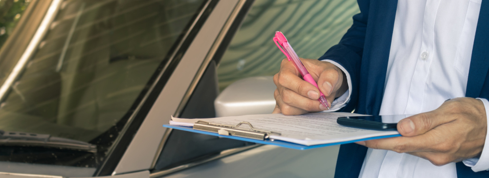 Insurance adjuster filling out a form on a clipboard next to a car