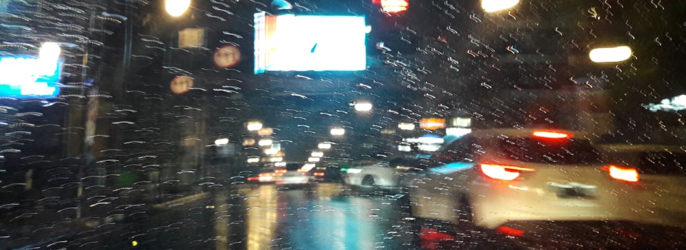 Photo from inside a car in the city at night with rain on the windshield and traffic outside