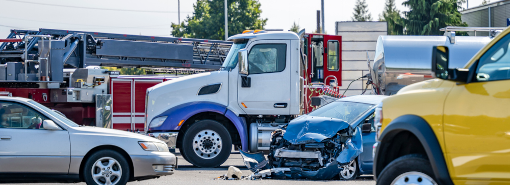 A severely damaged car after a head-on collision with a semi-truck at a city intersection