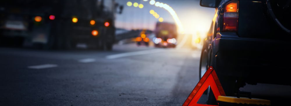 Red triangle warning sign set out next to an SUV on the side of the highway at dusk