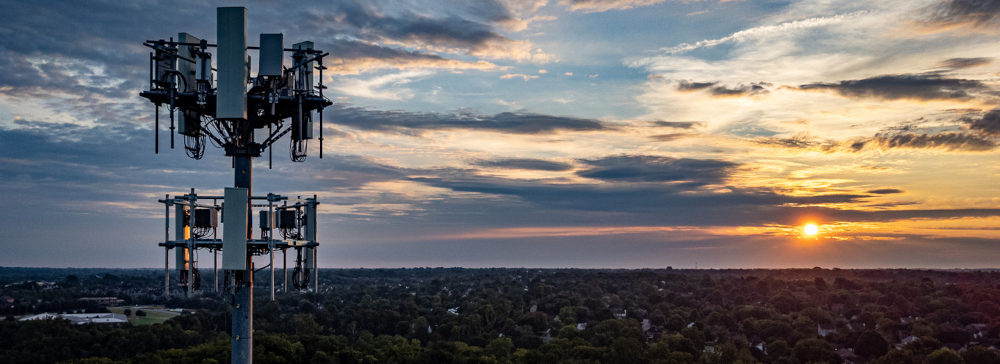 An aerial shot of a cellphone tower in the suburbs with a sunset in the background