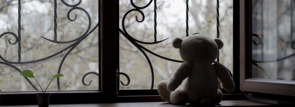 A stuffed bear sitting on a windowsill looking out at a dreary day