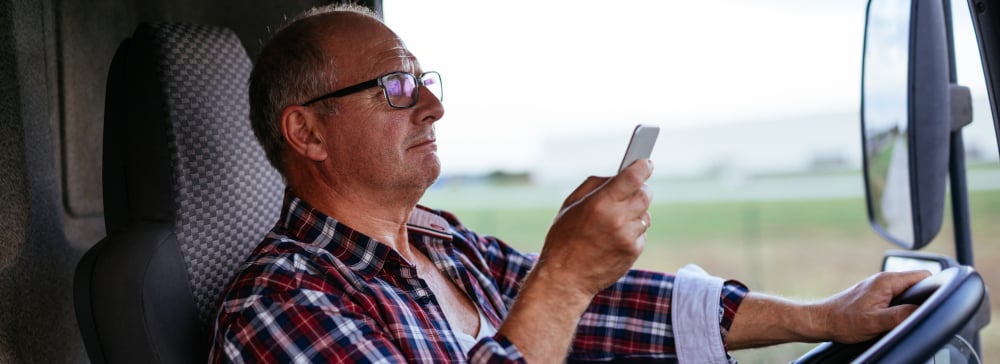 A man in the cab of a semi-truck texting while driving on the highway