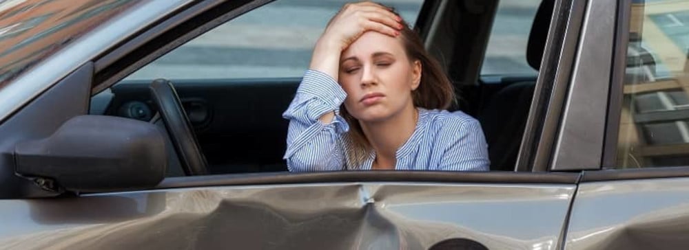 Woman in a car after an accident holding her forehead in pain