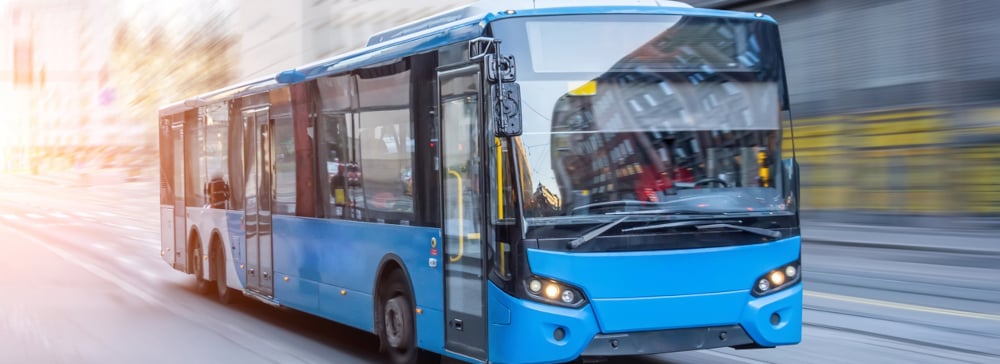 A blue bus driving down a city street in the early morning