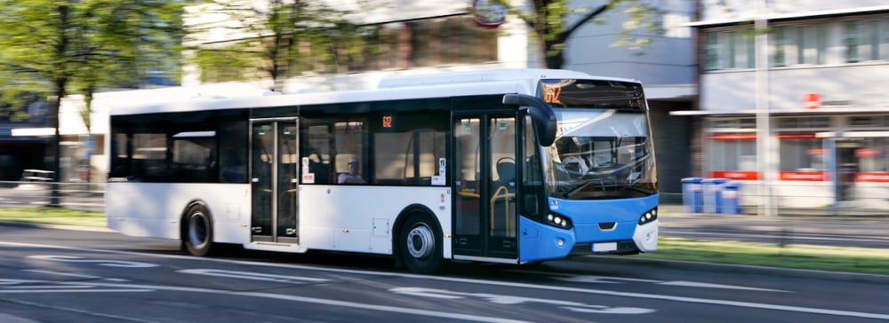 A blue and white city bus driving down a city street