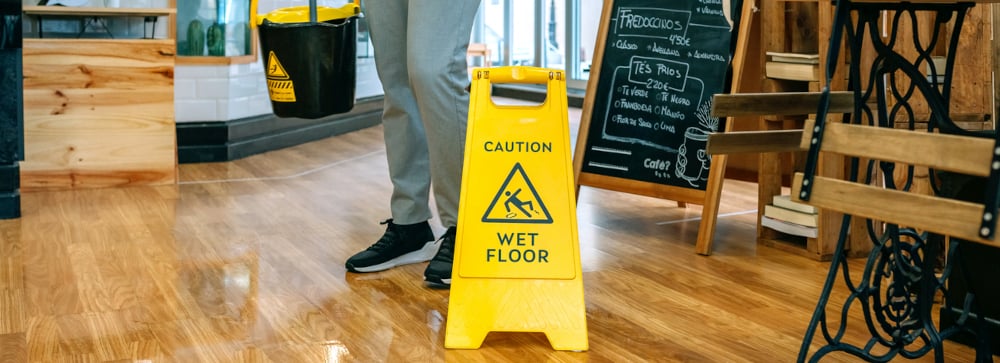 An employee placing a wet floor sign in the entryway of a business