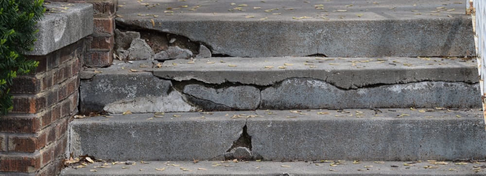 Cracked and broken cement stairs in front of a house