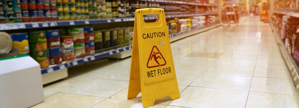 A yellow "Caution: Wet Floor" sign in a supermarket aisle