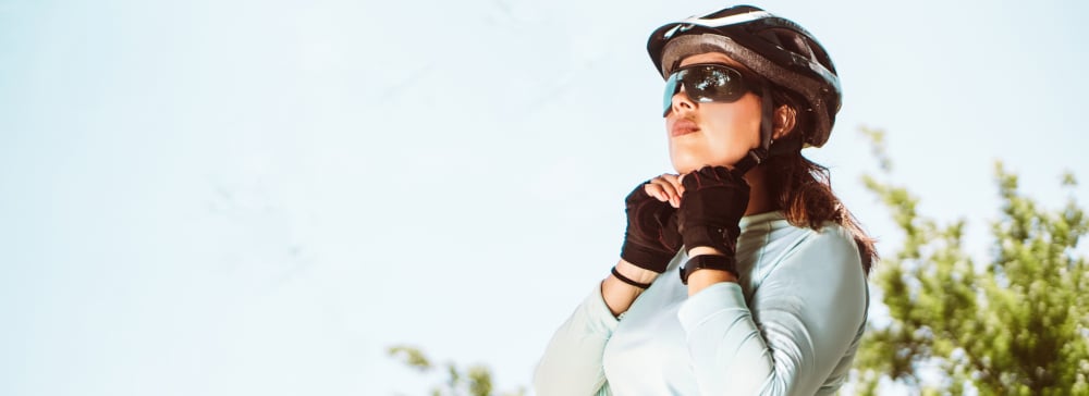 Cyclist woman with sportswear and sunglasses adjusting her bicycle helmet