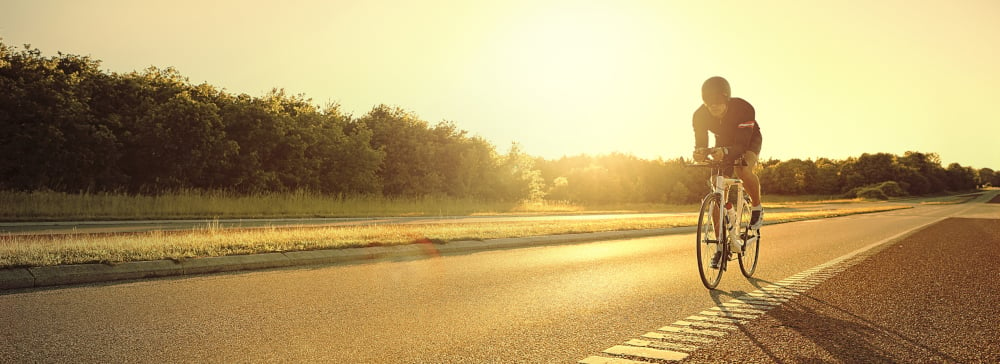 A bicyclist riding down the side of the road at sunset